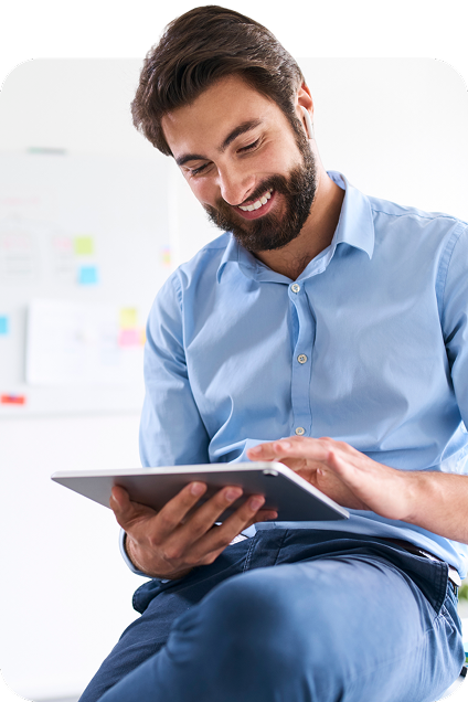 A man in an office setting sits and looks at a tablet in his hands.