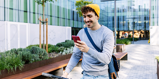 A man walking outside smiles and looks at his phone.