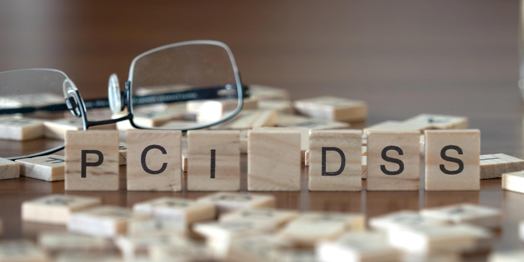 Scrabble tiles spell out "PCI DSS" on table with reading glasses and other scattered tiles