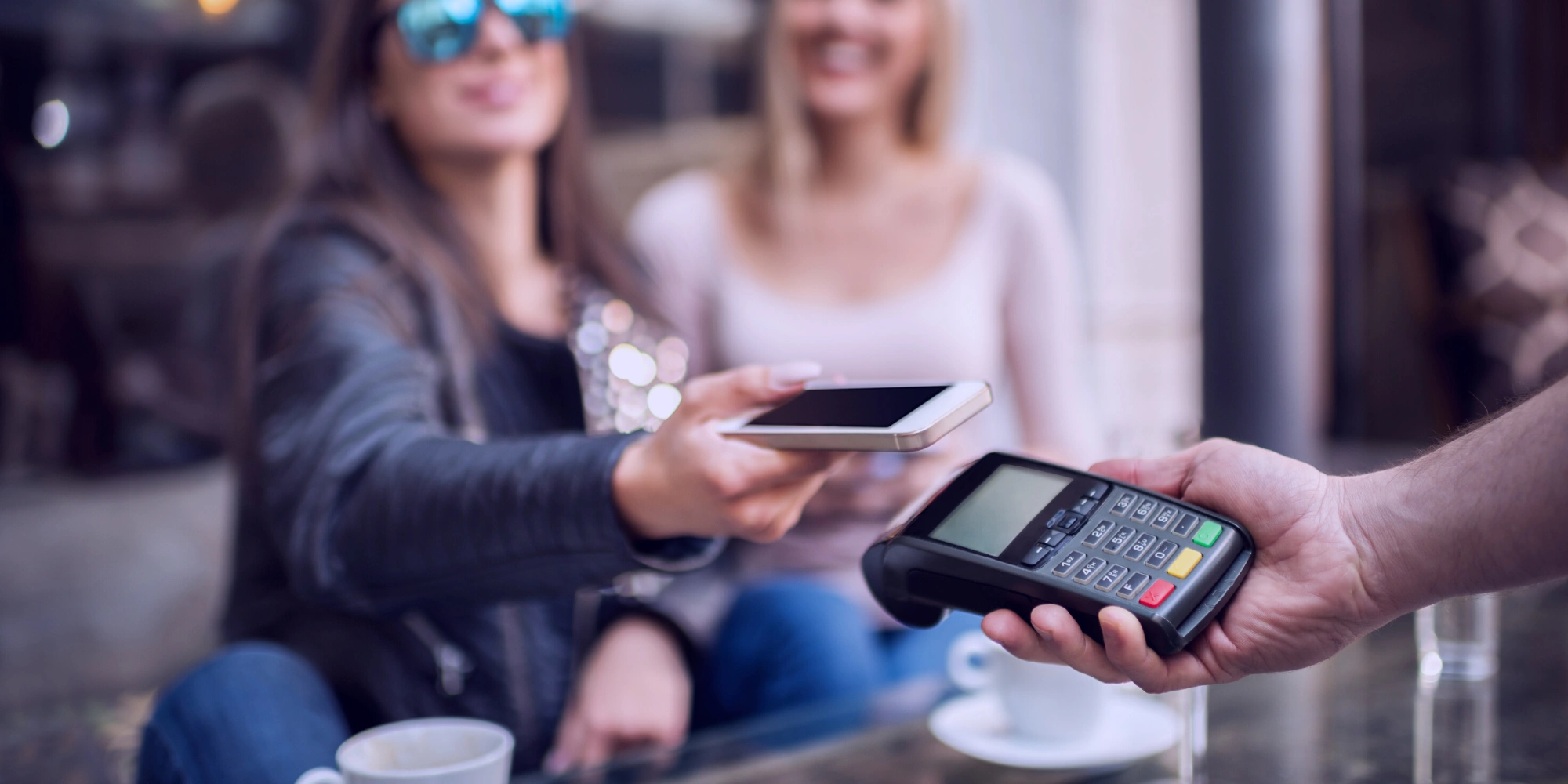 Customer in mirrored sunglasses uses smartphone to make contactless payment on handheld point of sale device