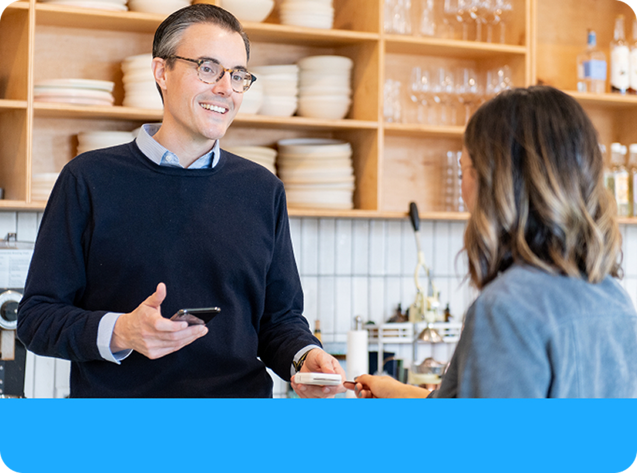 Owner of small business takes contactless payment from customer in retail setting.